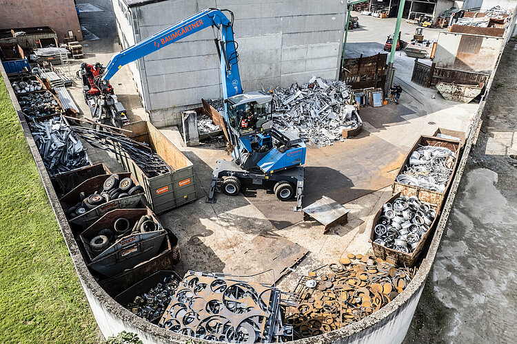 Ein Bagger mit Greifer bewegt Wertstoff auf einem Schrottplatz