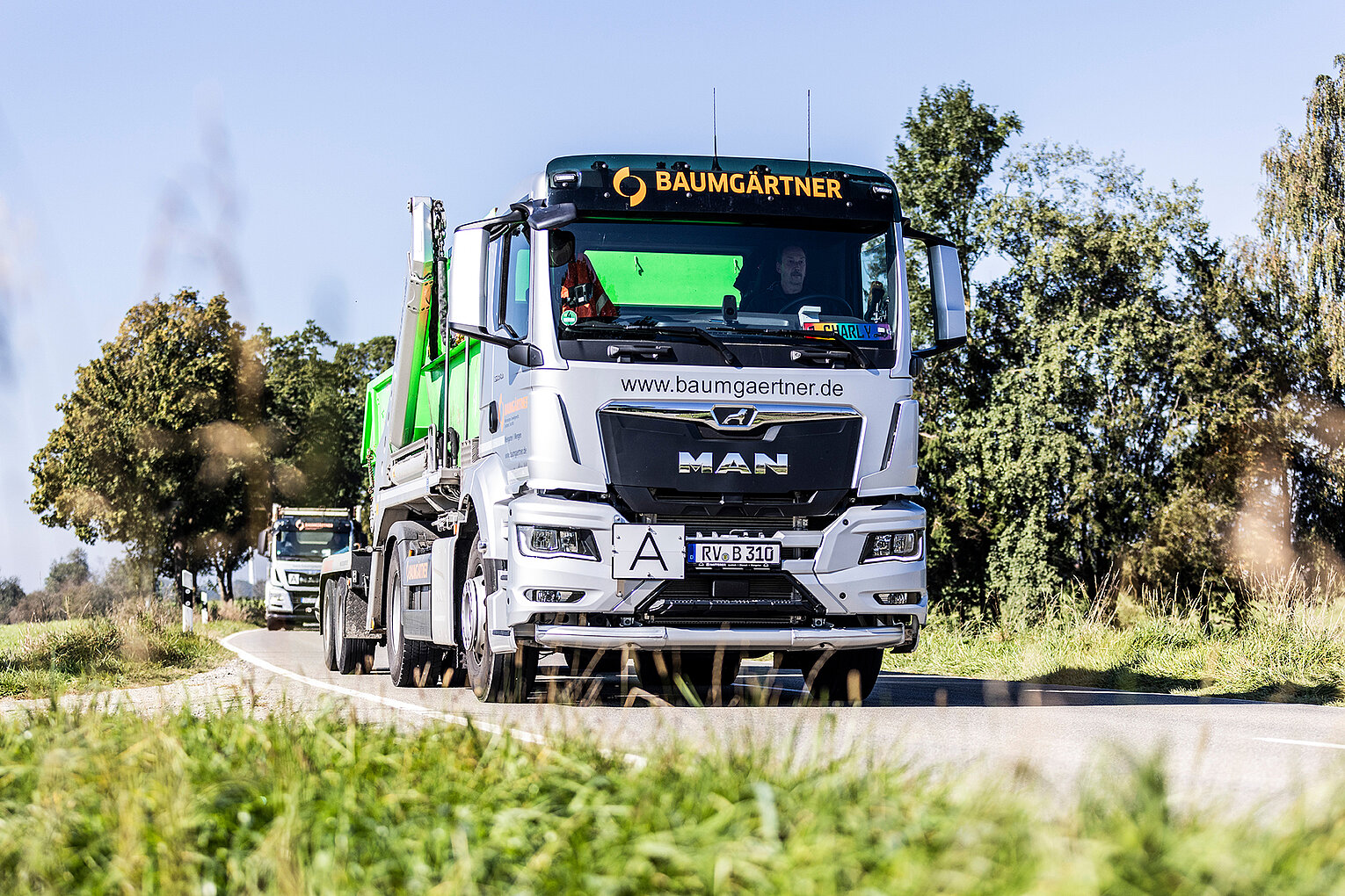 Baumgärtner LKW auf Landstraße Ein LKW von Baumgärtner mit aufgeladenem Container fährt auf einer Landstraße